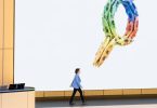 Conférencière marchant sur scène devant un écran géant affichant un logo Google formé de kayaks colorés, illustrant de manière créative les engagements de l'entreprise concernant la gestion de l'eau.