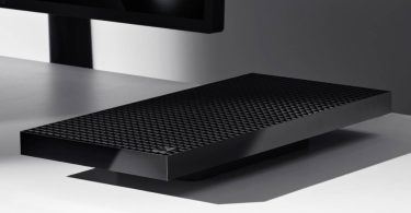 Vue en angle du mini-PC Microsoft Surface RTX Spark Dev Box en aluminium noir sur un bureau blanc. Le capot supérieur révèle une structure dense de 1 000 grilles d'aération géométriques sous un écran de contrôle.