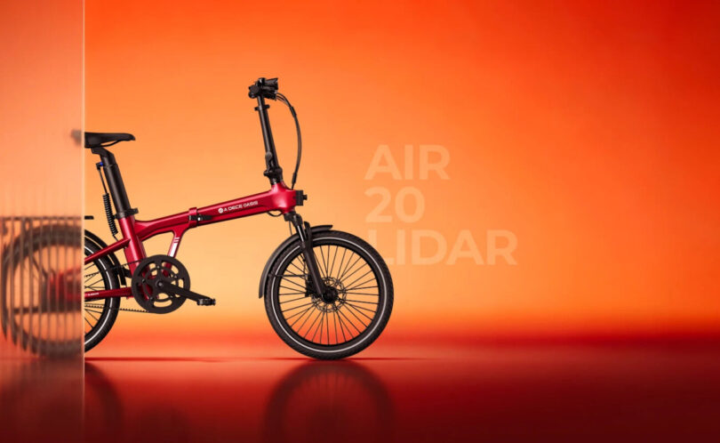 Vélo électrique pliant ADO Air 20 LiDAR rouge vu de profil sur fond orangé, roues de 20 pouces, fourche suspendue, freins à disque et transmission par courroie