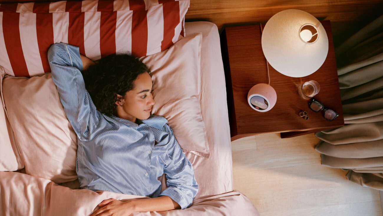 Femme endormie dans son lit à côté d'un réveil Amazon Echo Time posé sur la table de chevet, qui suit le sommeil par ultrasons sans caméra ni montre