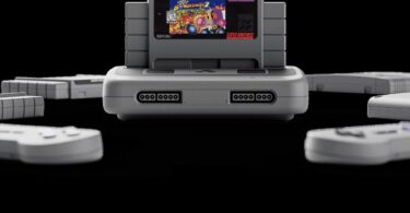 Console Analogue Super Nt+ grise avec une cartouche Super Nintendo insérée, entourée de manettes, nouvelle console rétro FPGA compatible cartouches originales en 1080p