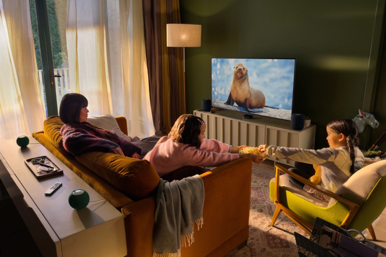 Famille installée dans un salon devant un téléviseur, avec l'Apple TV 4K et des enceintes HomePod formant un système de son surround