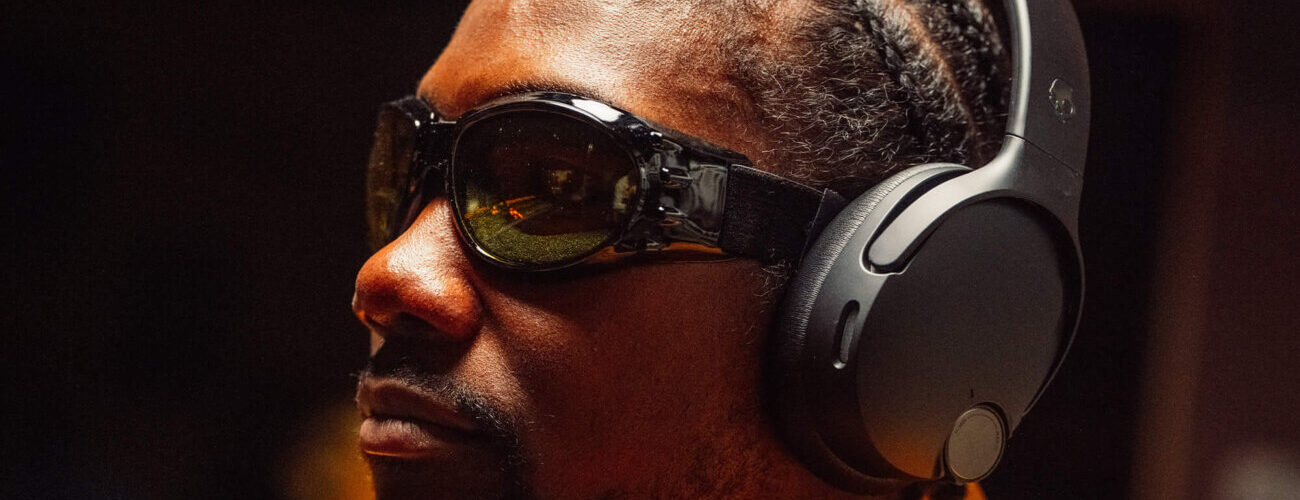 Homme portant le casque circum-auriculaire Skullcandy Crusher 1080 ANC noir, équipé de la réduction de bruit et de l'audio spatial Bose, illustration du rachat de Skullcandy par Bose