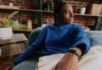 Homme assis dans un canapé portant au poignet le bracelet Bee Frontier noir, enregistreur à IA d'Amazon qui résume les conversations