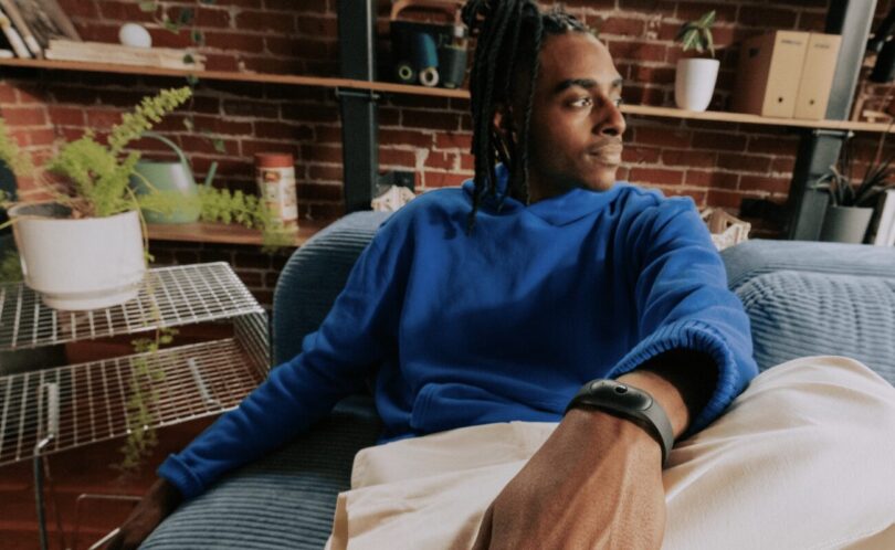 Homme assis dans un canapé portant au poignet le bracelet Bee Frontier noir, enregistreur à IA d'Amazon qui résume les conversations