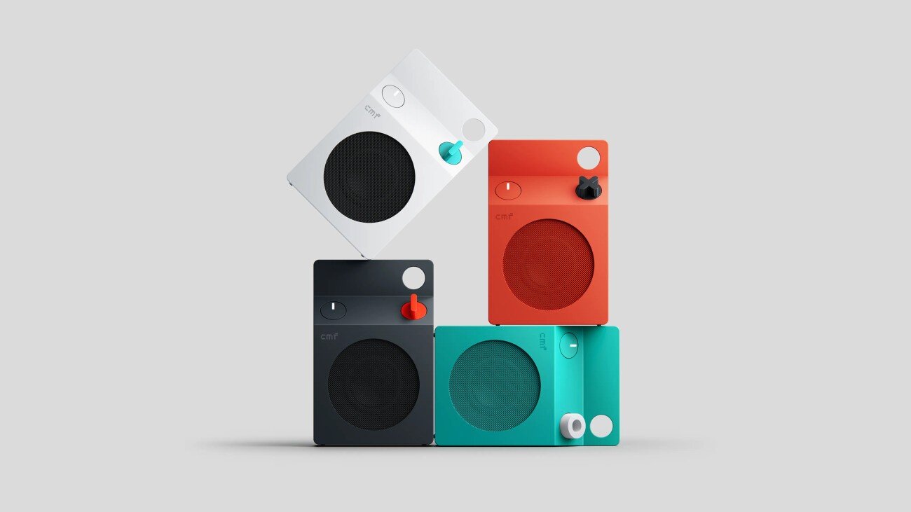 Quatre enceintes CMF Speaker S empilées en blanc, orange, gris foncé et turquoise, avec leur haut-parleur rond, leur molette et leurs boutons sur le dessus