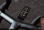 Le compteur vélo GPS Coros Dura 2 Solar fixé sur le cintre d'un vélo de route, écran tactile MiP de 3,5 pouces allumé avec vitesse, puissance et fréquence cardiaque