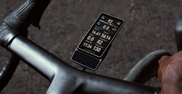 Le compteur vélo GPS Coros Dura 2 Solar fixé sur le cintre d'un vélo de route, écran tactile MiP de 3,5 pouces allumé avec vitesse, puissance et fréquence cardiaque