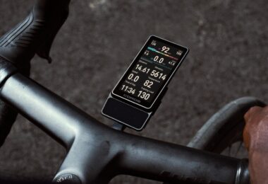 Le compteur vélo GPS Coros Dura 2 Solar fixé sur le cintre d'un vélo de route, écran tactile MiP de 3,5 pouces allumé avec vitesse, puissance et fréquence cardiaque