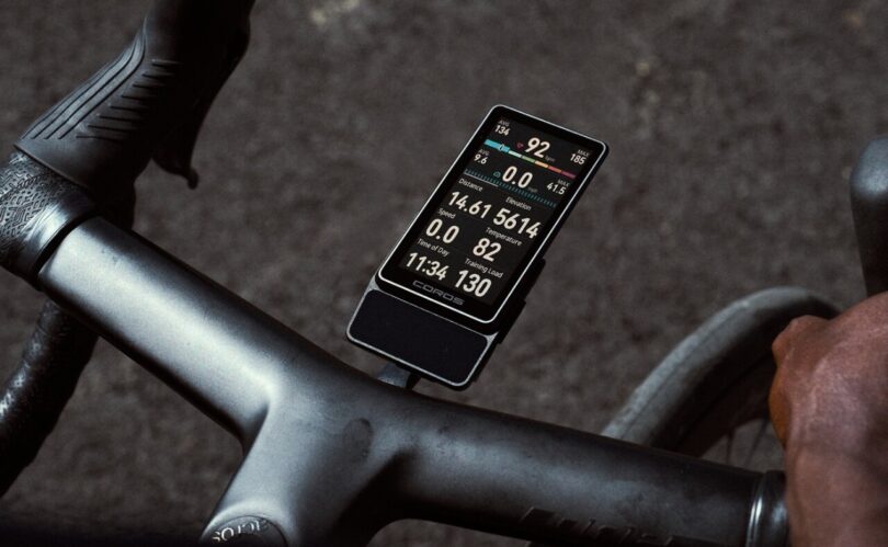 Le compteur vélo GPS Coros Dura 2 Solar fixé sur le cintre d'un vélo de route, écran tactile MiP de 3,5 pouces allumé avec vitesse, puissance et fréquence cardiaque
