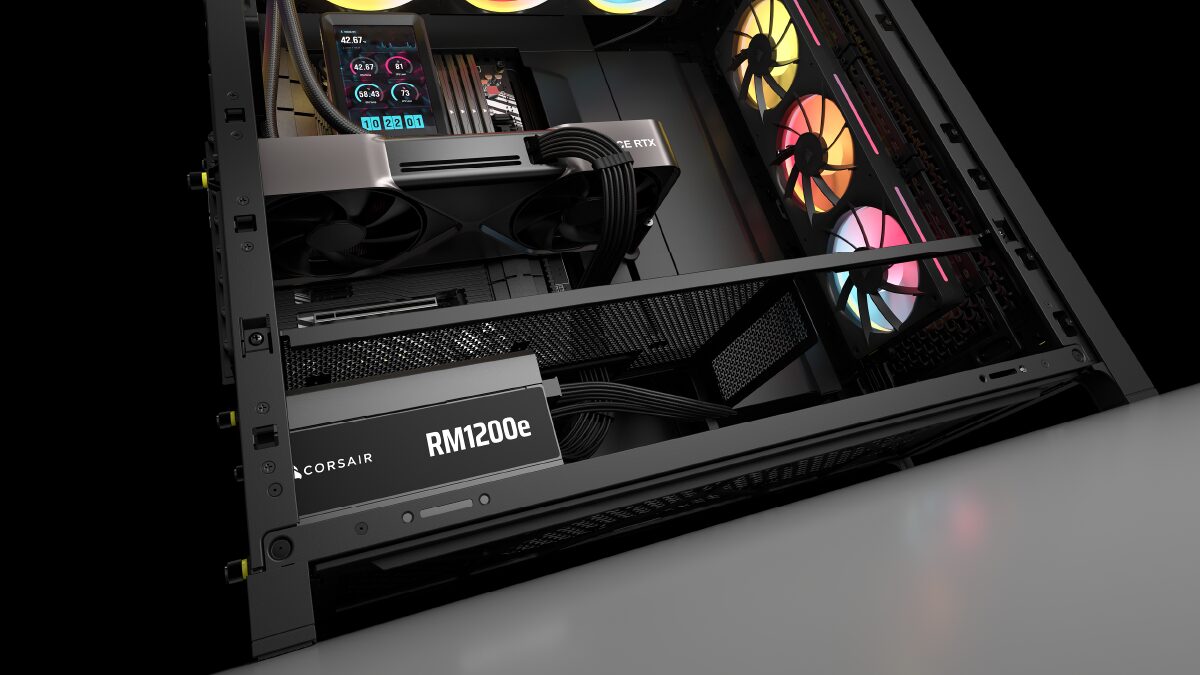 Alimentation Corsair RM1200e (2026) montée en bas d'un boîtier PC sous une carte graphique haut de gamme alimentée par un connecteur 12V-2x6