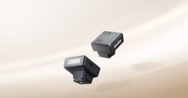 Deux mini flashs Godox iM10 noirs posés sur un fond beige, avec leur tube éclair frontal et leur pied de griffe porte-accessoire
