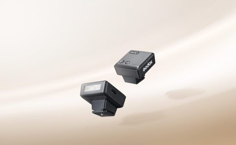Deux mini flashs Godox iM10 noirs posés sur un fond beige, avec leur tube éclair frontal et leur pied de griffe porte-accessoire