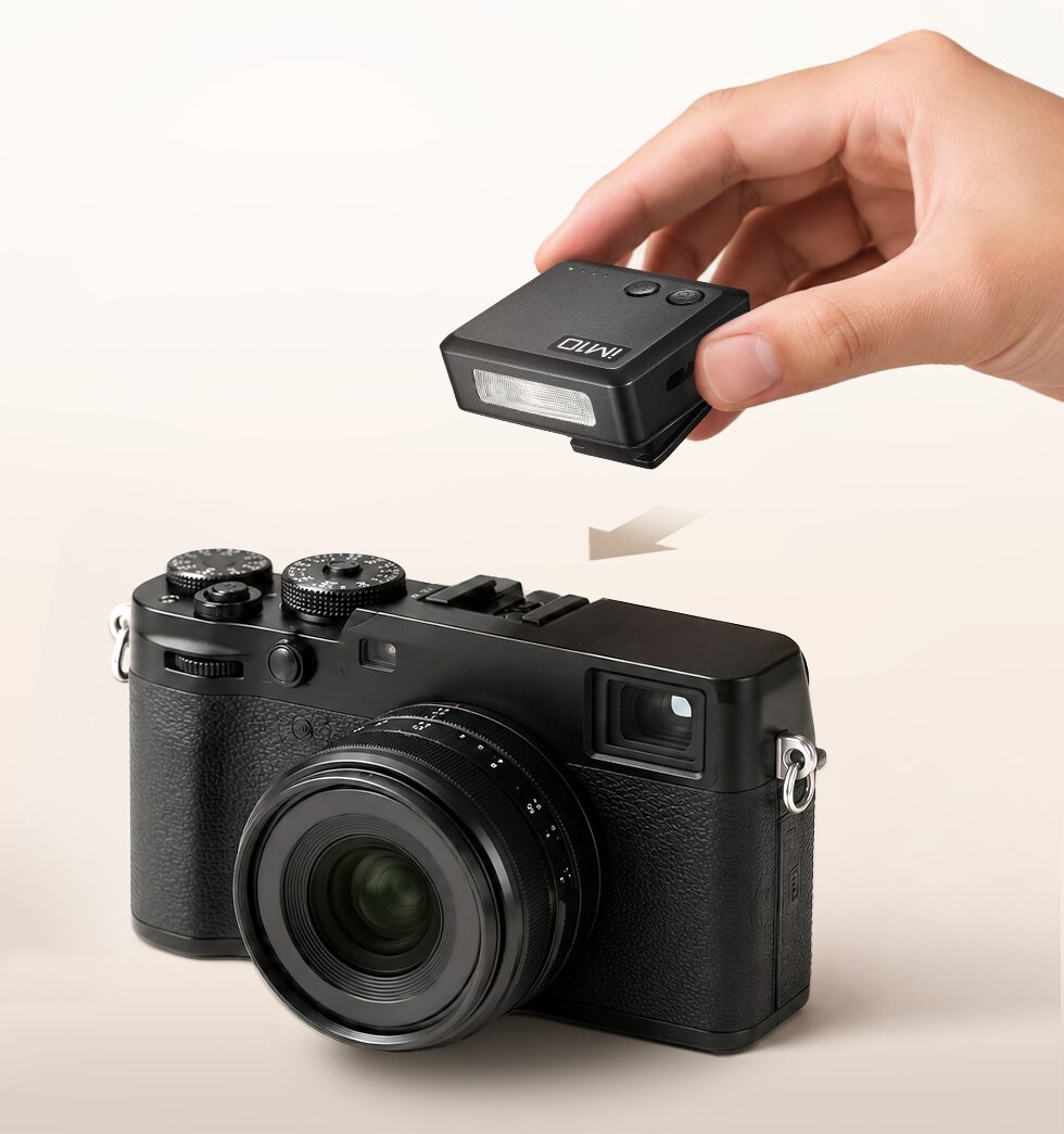 Une main installe le mini flash Godox iM10 sur la griffe porte-accessoire d'un appareil photo compact expert noir à objectif fixe