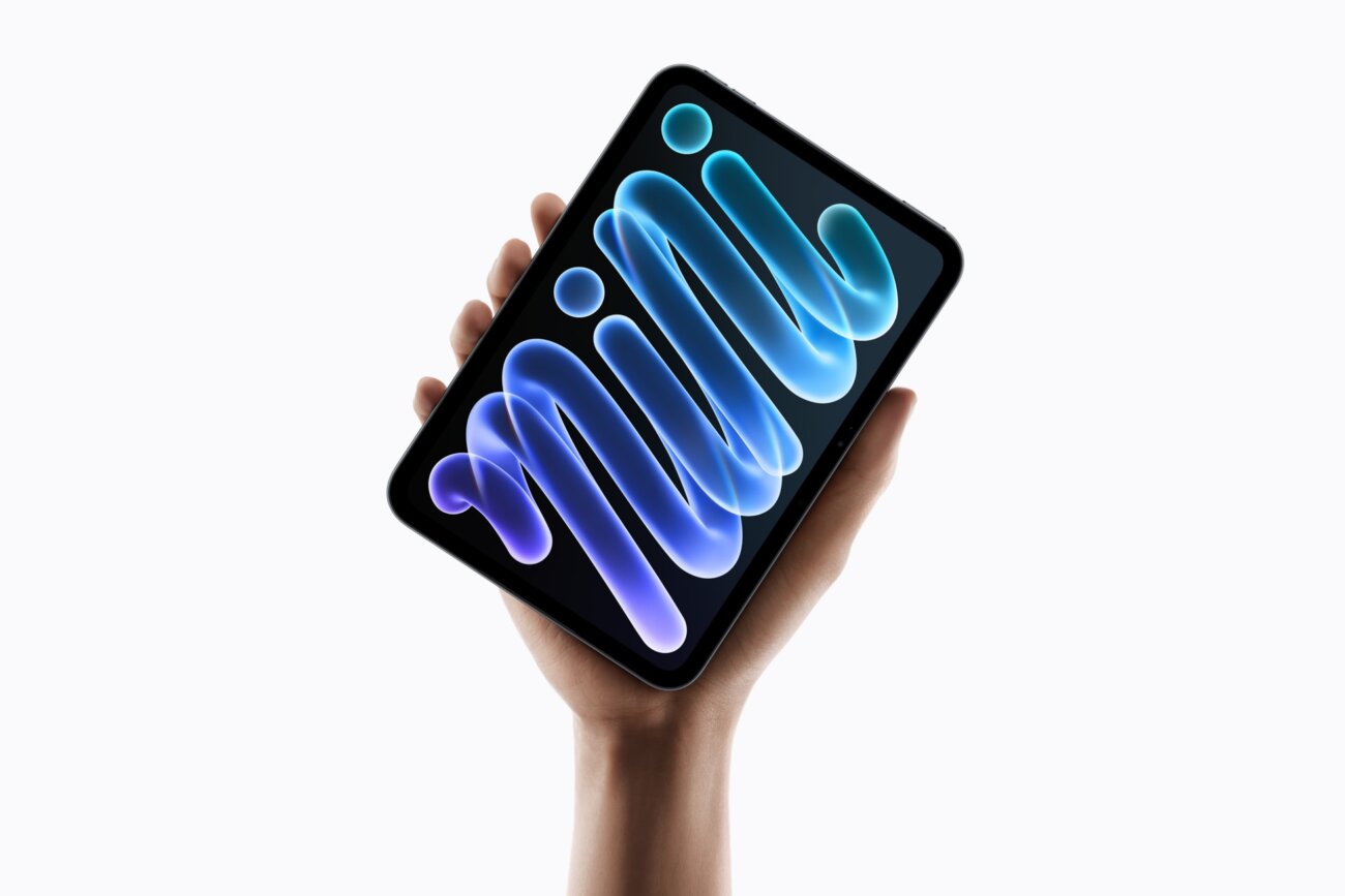 Une main tient le nouvel iPad mini A20 Pro, dont l'écran OLED de 8,5 pouces affiche un fond d'écran lumineux bleu et violet