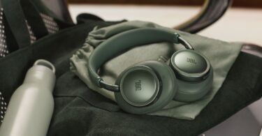 Casque sans fil JBL Live 780NC coloris vert à réduction de bruit adaptative, plié sur sa pochette de transport, posé sur un sac en velours vert à côté d'une gourde