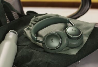 Casque sans fil JBL Live 780NC coloris vert à réduction de bruit adaptative, plié sur sa pochette de transport, posé sur un sac en velours vert à côté d'une gourde