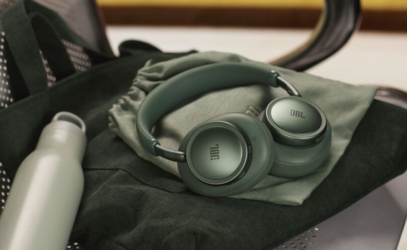 Casque sans fil JBL Live 780NC coloris vert à réduction de bruit adaptative, plié sur sa pochette de transport, posé sur un sac en velours vert à côté d'une gourde