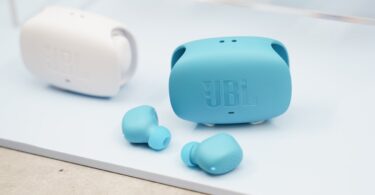 Écouteurs sans fil JBL Wave Buds 3 coloris bleu canard posés devant leur boîtier de charge à double ouverture latérale, avec un second boîtier blanc en arrière-plan