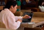 Utilisateur touchant du doigt l'écran OLED tactile du MacBook Pro PROLED XDR posé sur une table, premier Mac à écran tactile