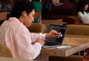 Utilisateur touchant du doigt l'écran OLED tactile du MacBook Pro PROLED XDR posé sur une table, premier Mac à écran tactile