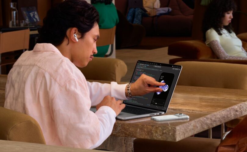 Utilisateur touchant du doigt l'écran OLED tactile du MacBook Pro PROLED XDR posé sur une table, premier Mac à écran tactile