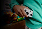 Manette XBOX Nano blanche glissée dans la poche d'un sweat vert, devant une TV affichant un jeu, illustrant le format de poche de la nouvelle manette Xbox pour le cloud gaming