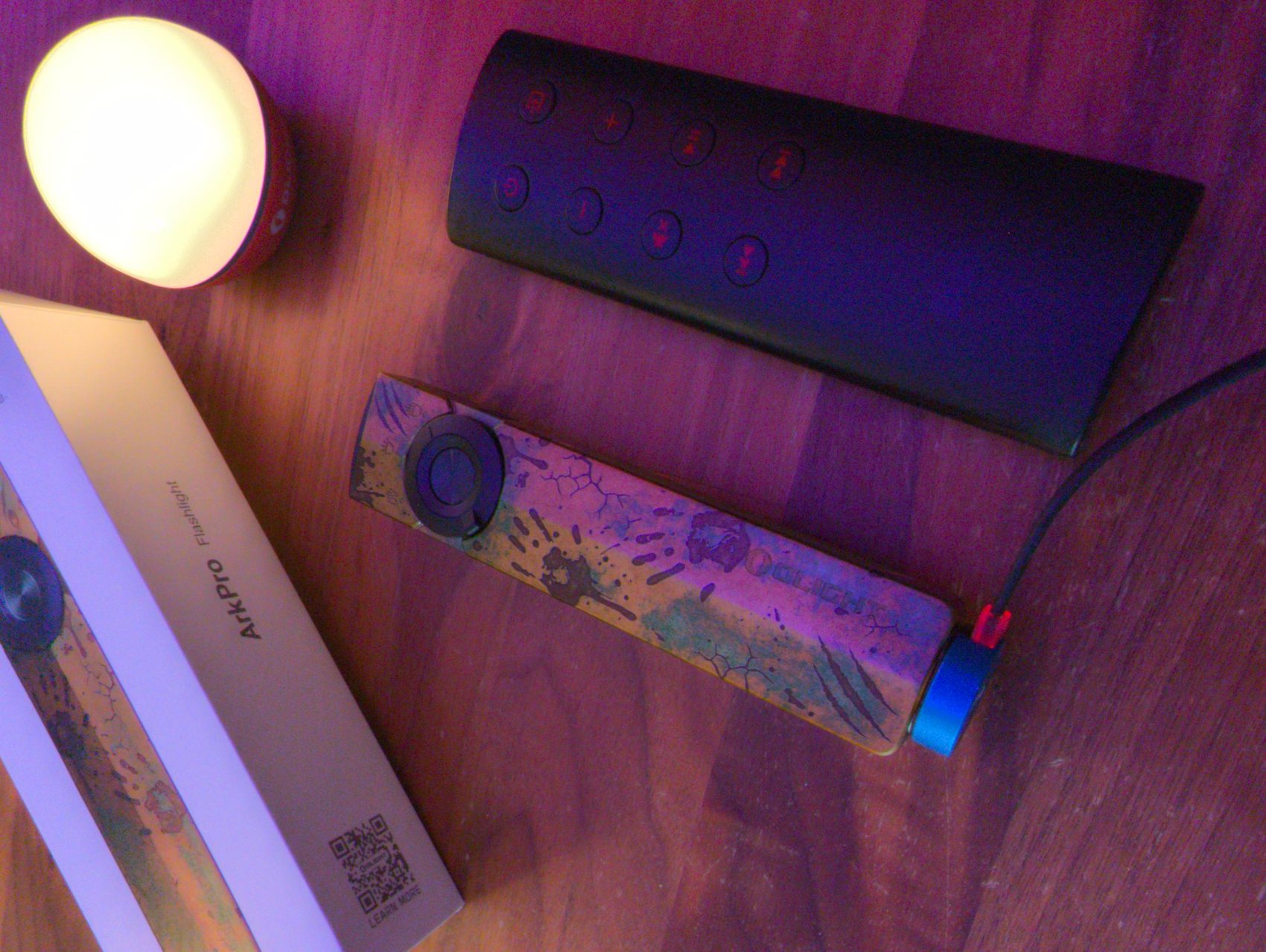 Olight ArkPro en charge posée à côté d'une télécommande d'enceintes KEF et de la lampe boule Olight Obulb