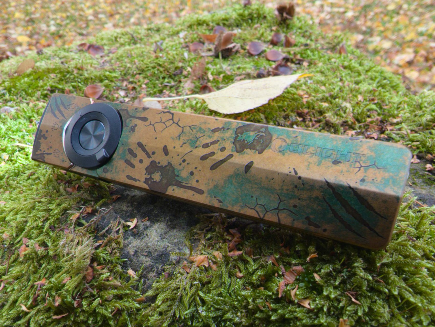 Face avant de l'Olight ArkPro Ultra Relique des terres désolées avec son sélecteur rotatif, posée sur la mousse