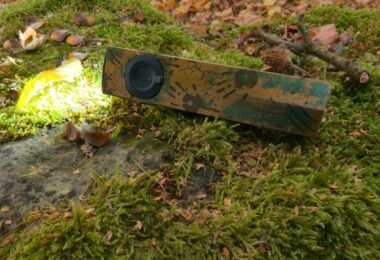 Olight ArkPro Ultra édition Relique des terres désolées allumée en Pure Flood, posée sur un rocher moussu en automne