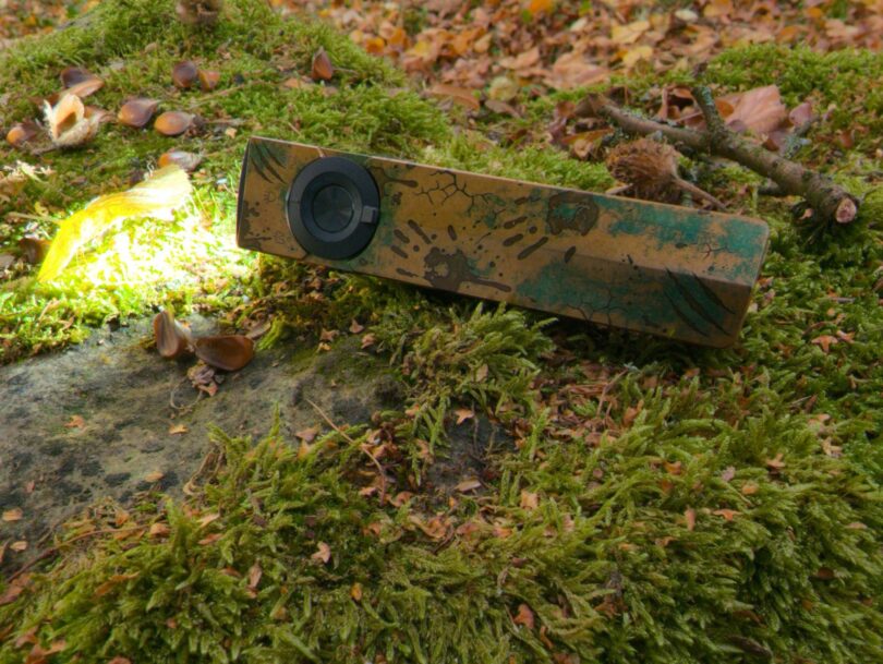 Olight ArkPro Ultra édition Relique des terres désolées allumée en Pure Flood, posée sur un rocher moussu en automne