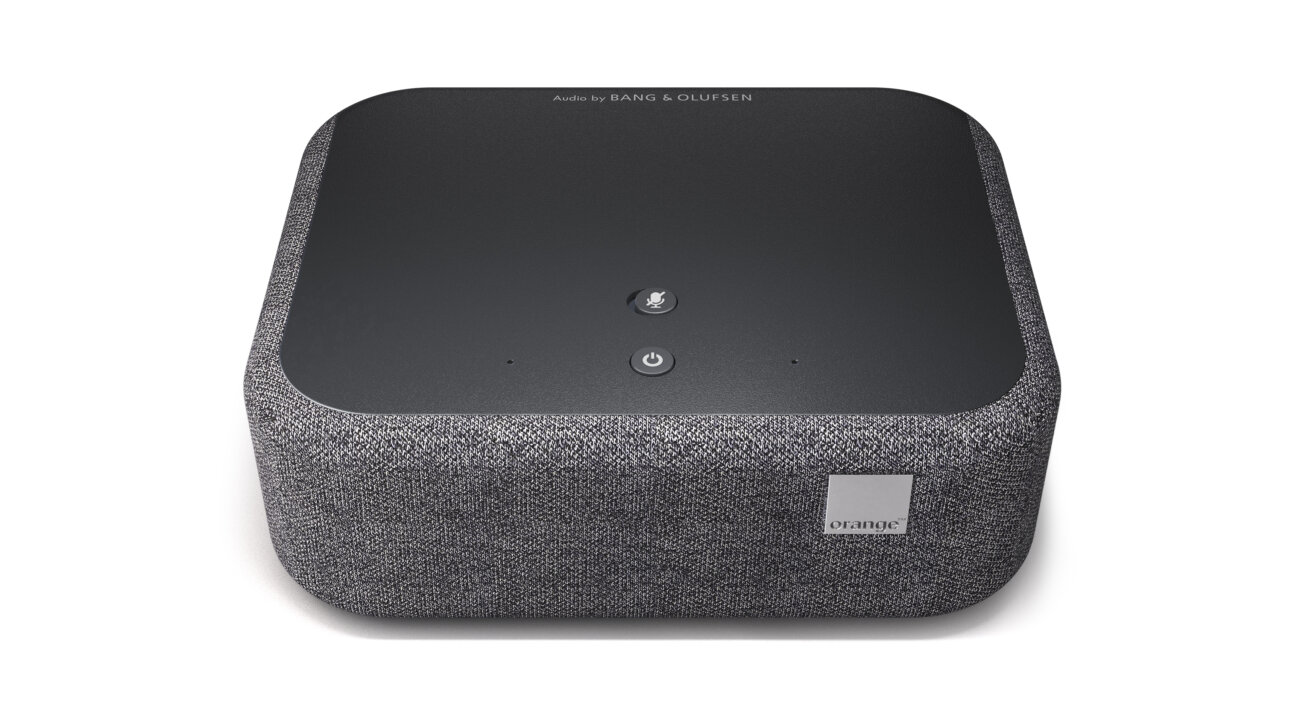 Le Décodeur Home Cinema d'Orange vu de dessus avec son capot noir marqué Audio by Bang & Olufsen, ses boutons micro et marche et son habillage en tissu gris