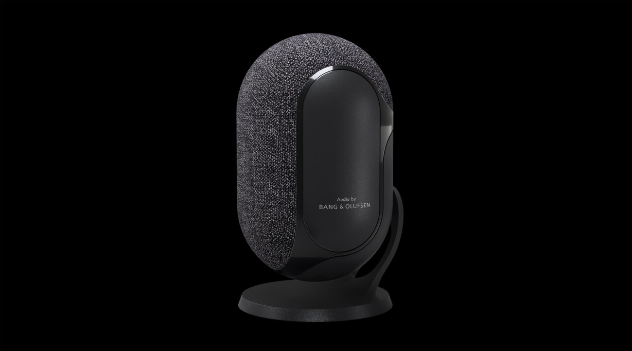Enceinte sans fil Dolby Atmos FlexConnect d'Orange en forme d'ovale, habillée de tissu gris et posée sur un pied noir, avec la mention Audio by Bang & Olufsen