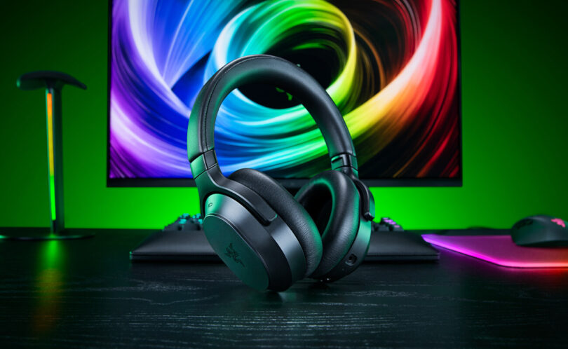 Casque gaming sans fil Razer Barracuda V2 Pro noir posé sur un bureau devant un écran coloré, avec clavier et souris Razer en arrière-plan