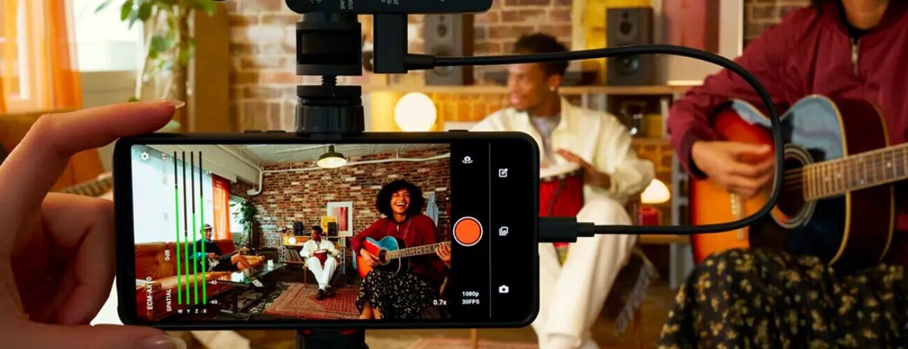 Le micro Sony ECM-AX10 branché en USB-C sur un smartphone fixé sur trépied, utilisé pour filmer des musiciens en audio spatial dans un salon