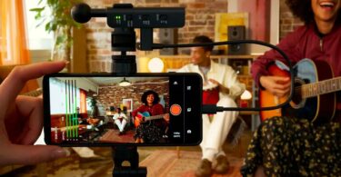 Le micro Sony ECM-AX10 branché en USB-C sur un smartphone fixé sur trépied, utilisé pour filmer des musiciens en audio spatial dans un salon