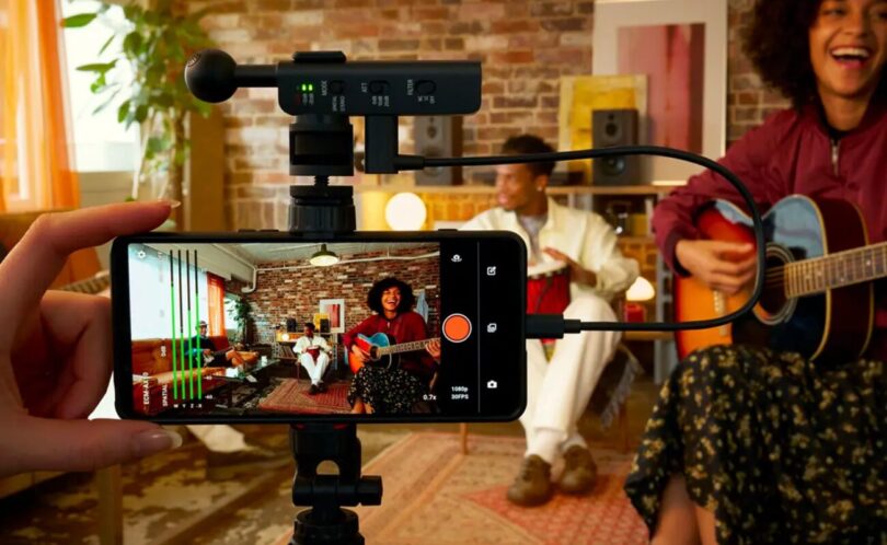 Le micro Sony ECM-AX10 branché en USB-C sur un smartphone fixé sur trépied, utilisé pour filmer des musiciens en audio spatial dans un salon