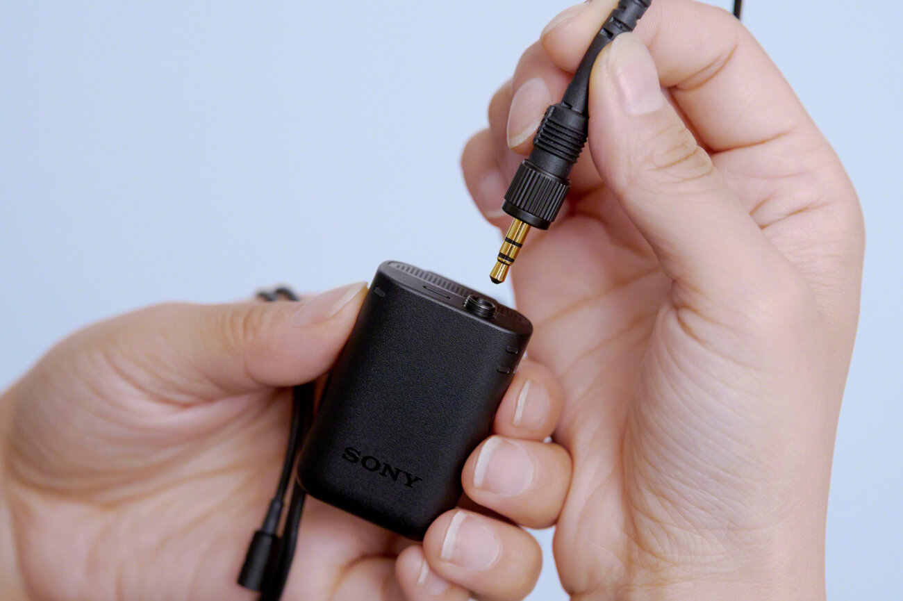 Main branchant la fiche jack 3,5 mm d'un micro-cravate dans l'émetteur noir Sony ECM-W5T, entrée micro verrouillable