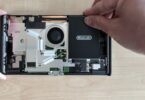 Intérieur de la Nintendo Switch 2 révisée BEE-001(-01) ouverte, avec le ventilateur, les caloducs, la carte mère et la batterie noire Nintendo que l'on soulève sans adhésif