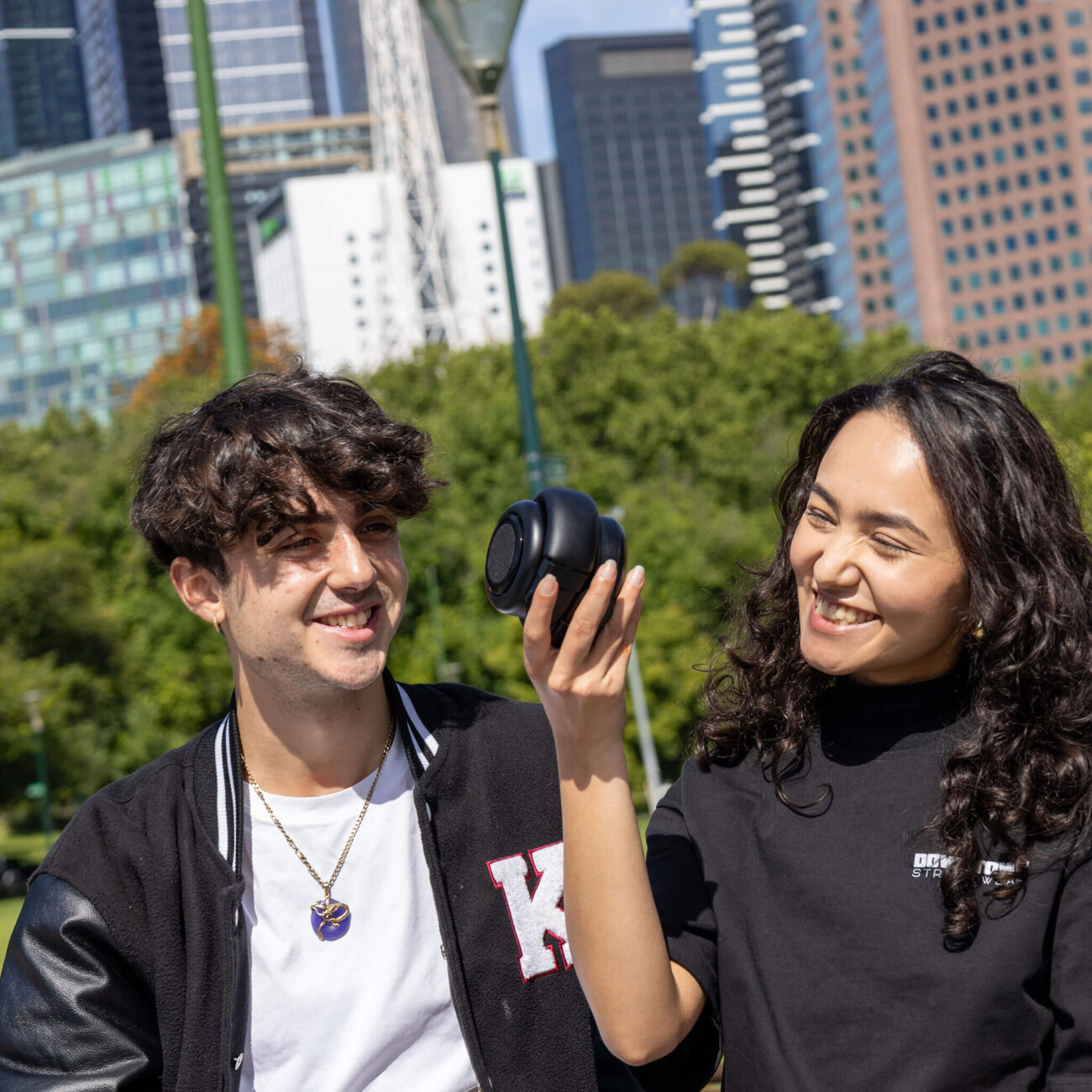 Deux jeunes adultes en ville écoutant de la musique sur le TDM Neo utilisé en mode enceinte Bluetooth, tenu à la main