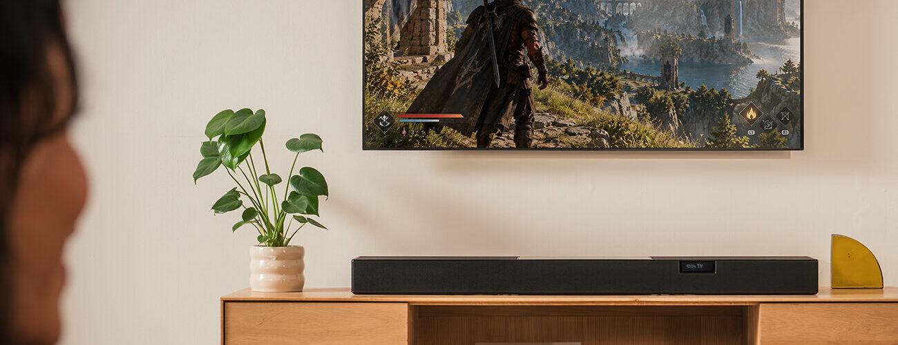Barre de son Teufel Cinebar Pro 2 noire posée sur un meuble TV en bois sous un téléviseur, barre Dolby Atmos 5.1.2 à dix haut-parleurs