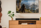 Barre de son Teufel Cinebar Pro 2 noire posée sur un meuble TV en bois sous un téléviseur, barre Dolby Atmos 5.1.2 à dix haut-parleurs