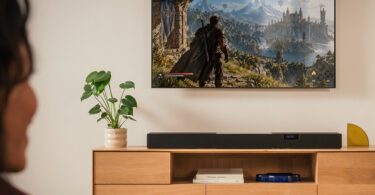 Barre de son Teufel Cinebar Pro 2 noire posée sur un meuble TV en bois sous un téléviseur, barre Dolby Atmos 5.1.2 à dix haut-parleurs