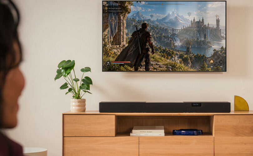 Barre de son Teufel Cinebar Pro 2 noire posée sur un meuble TV en bois sous un téléviseur, barre Dolby Atmos 5.1.2 à dix haut-parleurs