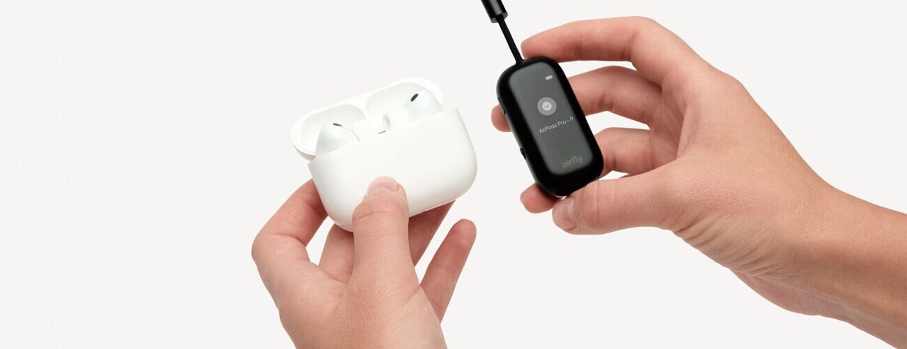 L'adaptateur Bluetooth Twelve South AirFly View noir tenu en main à côté d'un boîtier d'AirPods Pro, avec son écran qui guide l'appairage des écouteurs sans fil