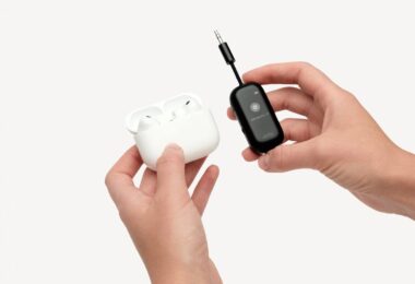 L'adaptateur Bluetooth Twelve South AirFly View noir tenu en main à côté d'un boîtier d'AirPods Pro, avec son écran qui guide l'appairage des écouteurs sans fil