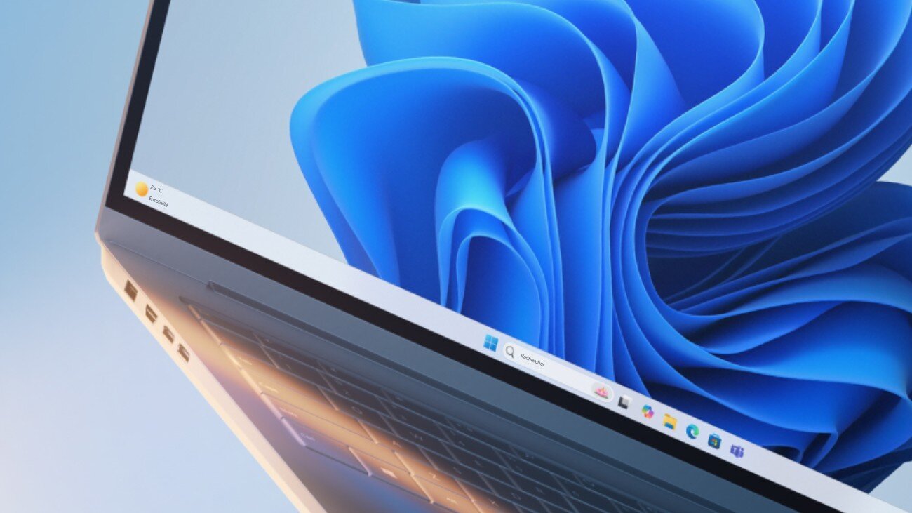 Ordinateur portable ouvert affichant le bureau de Windows 11 avec son fond d'écran bleu en forme de fleur et la barre des tâches centrée