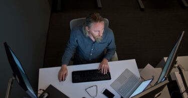 Un utilisateur devant un poste de travail Windows équipé de plusieurs écrans, d'un clavier et d'un ordinateur portable, illustration des mises à jour de sécurité Windows