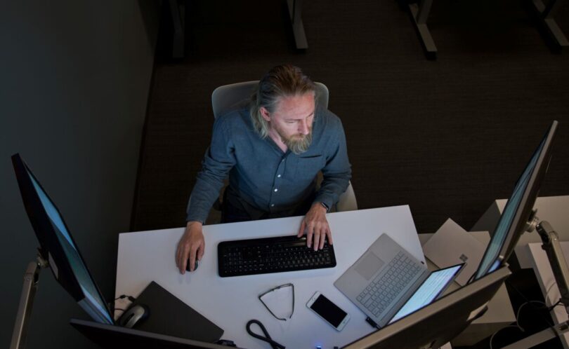 Un utilisateur devant un poste de travail Windows équipé de plusieurs écrans, d'un clavier et d'un ordinateur portable, illustration des mises à jour de sécurité Windows