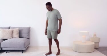 Homme se pesant pieds nus sur une balance connectée Withings Body Smart blanche dans un salon lumineux, illustration de la synchronisation des données avec Apple Santé